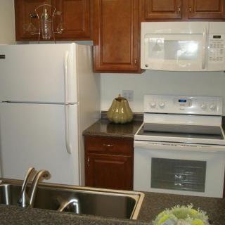 A modern kitchen featuring a refrigerator, microwave, and oven with wooden cabinets.