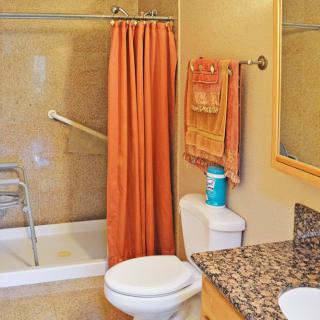 An accessible bathroom with a shower, orange shower curtain, toilet, towels, and grab bar.
