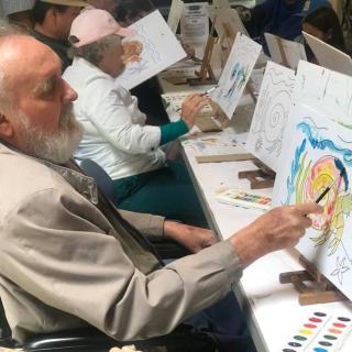 Elderly individuals participating in a group art class, engaging in painting activities.