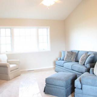 A cozy living room with a blue sofa set, armchair, and large windows allowing natural light.
