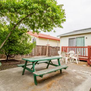 A cozy outdoor patio with a picnic table, chairs, and a tree providing shade.