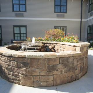 A stone fountain surrounded by a circular brick wall in a courtyard setting.
