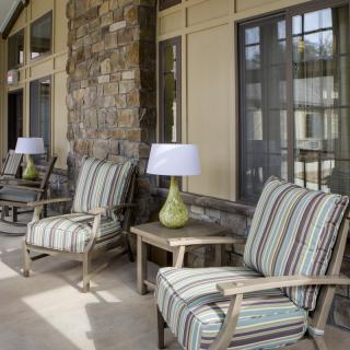 A cozy patio with striped cushioned chairs and small tables with lamps, set against a stone wall.