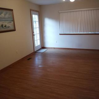 An empty room with wooden flooring, a door, window blinds, and a painting on the wall.