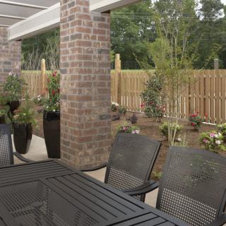 A cozy patio area with chairs and a table, surrounded by a garden and wooden fence.