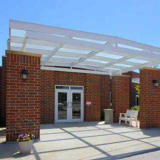 A brick building entrance with a pergola and outdoor seating.