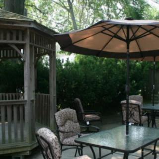 An outdoor patio area featuring a gazebo, tables with umbrellas, and cushioned chairs.