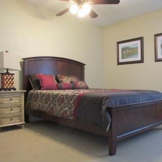 A cozy bedroom featuring a wooden bed with patterned bedding, a nightstand with a lamp, and artwork on the walls.