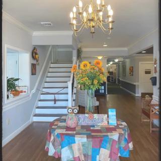 A welcoming foyer with a chandelier, staircase, and a table decorated with flowers and a colorful tablecloth.