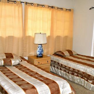 A cozy bedroom with two twin beds, a nightstand, and a lamp by the window.