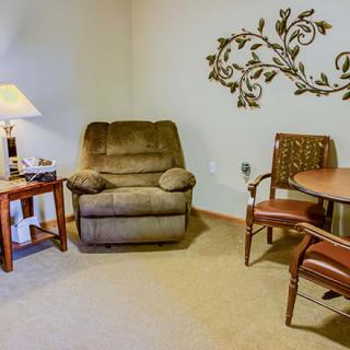 A cozy living room corner with an armchair, side table, lamp, and decorative wall art.