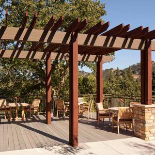 An inviting outdoor patio featuring a wooden pergola, with tables and chairs set up for relaxation amid a scenic tree view.