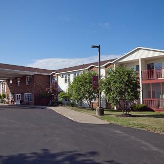 Exterior view of a residential apartment building with a driveway and trees under a clear blue sky.