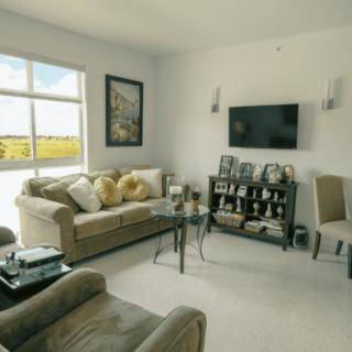 A cozy living room featuring comfortable sofas, an armchair, a large window with scenic views, and a wall-mounted television.