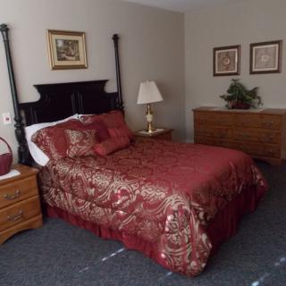 A well-decorated bedroom featuring a bed with red bedding, a side table with a lamp, and framed art on the walls.