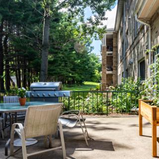 A peaceful outdoor patio setup featuring a grill and seating, surrounded by greenery.