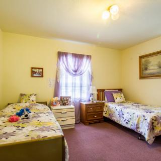A cozy bedroom features two twin beds with floral bedding, a shared nightstand, and decorative curtains on the window.