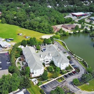 Aerial view of a large building surrounded by trees with a nearby lake and parking lot.
