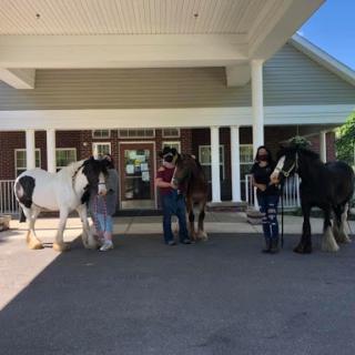 A group of people stand with their horses in front of a building on a sunny day.