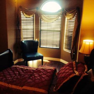 A cozy bedroom with elegant drapes, a comfortable chair by the window, and warm lighting.