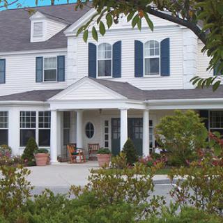 A charming white house with blue shutters and a welcoming front porch, surrounded by lush greenery.