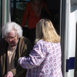 An elderly woman receiving assistance while getting off a bus.