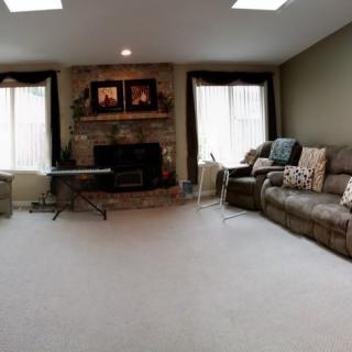 A cozy living room with a fireplace, large sofa, and natural light from windows.