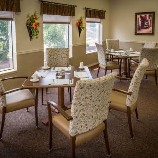 A cozy dining room with arranged tables and chairs, decorated with floral accents.