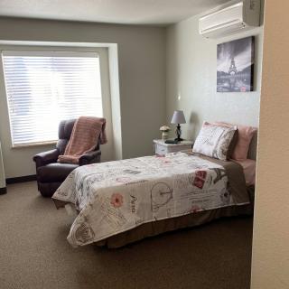 A cozy bedroom with a single bed, an armchair by the window, and a nightstand with a lamp.