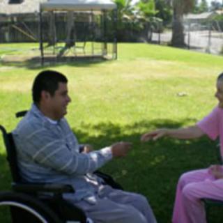 A person in a wheelchair interacting with a caregiver in a park setting.