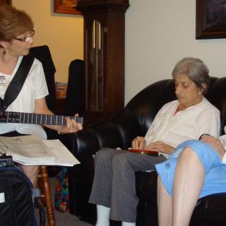 A group of people sitting in a living room, with one person playing a guitar.