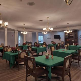 A spacious dining room with green tablecloths and elegant chandeliers.