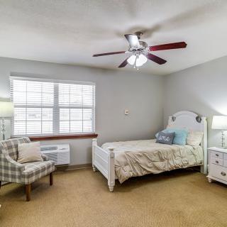 A cozy bedroom with a single bed, ceiling fan, and armchair.