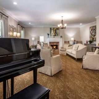 A spacious living room featuring a grand piano, fireplace, and elegant furnishings.