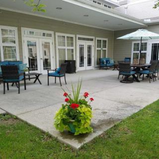 A cozy patio area with outdoor seating, tables, and an umbrella, surrounded by greenery and flowers.