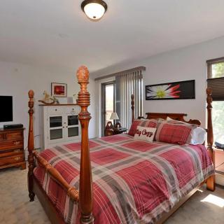 A cozy bedroom featuring a four-poster bed with plaid bedding, wooden furniture, and soft lighting.