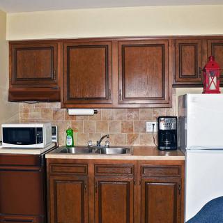 A compact kitchen area with wooden cabinets, a microwave, sink, refrigerator, and coffee maker.