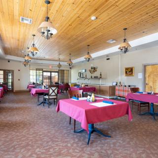 A spacious dining room with red tablecloths and wooden ceiling.