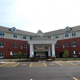 A modern hospital building with a brick facade and an entrance leading to a covered drop-off area, surrounded by a parking lot.