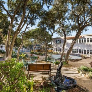 A peaceful garden with benches surrounded by trees and a building in the background.