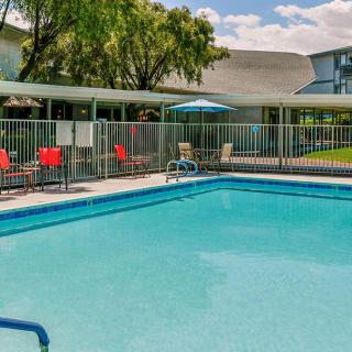An outdoor swimming pool surrounded by a fence with chairs and an umbrella nearby.
