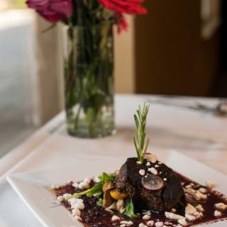 A beautifully plated gourmet dish served at an elegant restaurant, with a floral centerpiece in the background.