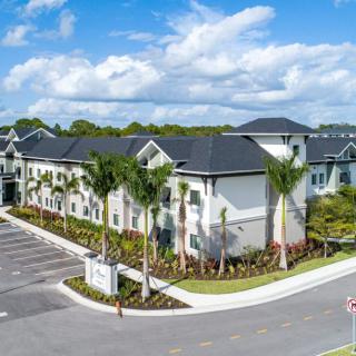 A modern building surrounded by palm trees and a neatly landscaped parking lot under a blue sky with clouds.
