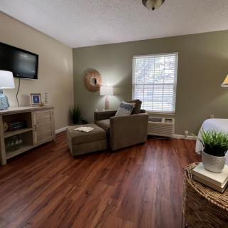 A cozy living room with wood flooring, featuring a comfortable armchair and a television mounted on the wall.