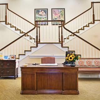 A stylish office interior featuring a wooden desk, decorative art pieces, and a grand staircase.