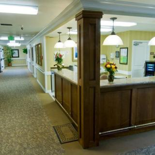 A well-lit reception area with a wooden counter and decorative flowers in an office hallway.