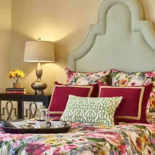 A stylish bedroom featuring floral bedding and decorative pillows, complemented by a modern table lamp and cozy decor.
