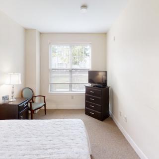 A cozy bedroom with a bed, dresser, and TV near a window.