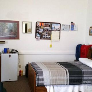 A cozy dorm room with a neatly made bed and personal decorations on the walls.
