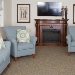 A cozy living room with blue armchairs, a wooden fireplace, and a mounted television.
